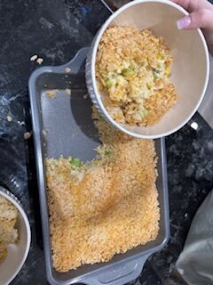 Pouring creamy chicken and rice filling into a baking pan with crispy Rice Krispie topping