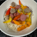 Polish kielbasa with peppers and onions served over rice in a white bowl