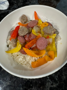 Polish kielbasa with peppers and onions served over rice in a white bowl