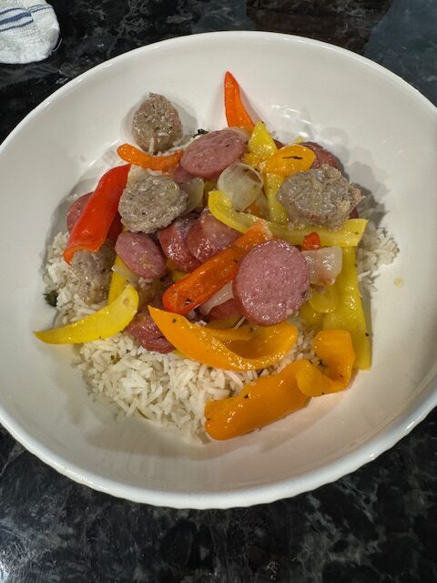 Polish kielbasa with peppers and onions served over rice in a white bowl