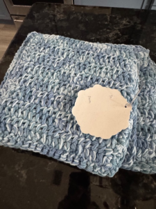 Handmade crochet kitchen gift set with dishcloth, hot pad, and drying mat together with a gift tag.