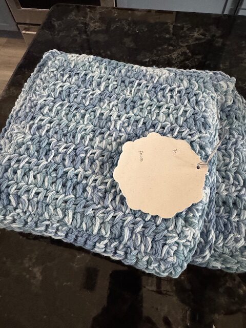 Handmade crochet kitchen gift set with dishcloth, hot pad, and drying mat together with a gift tag.