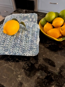 Crochet dishcloth and hot pad in blue cotton yarn with fresh lemon on top