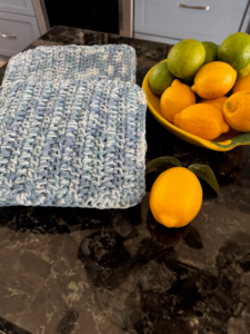 Blue crochet dishcloth and hot pad set styled beside a bowl of lemons and limes