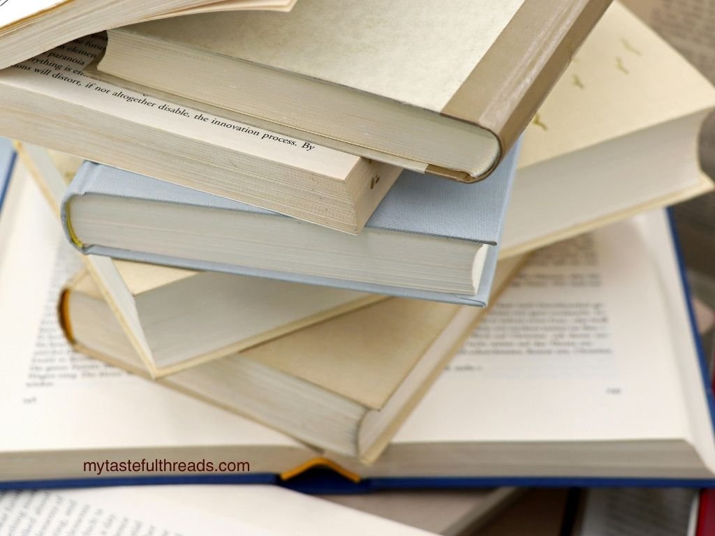 Stack of hardcover books piled on top of an open book viewed from above